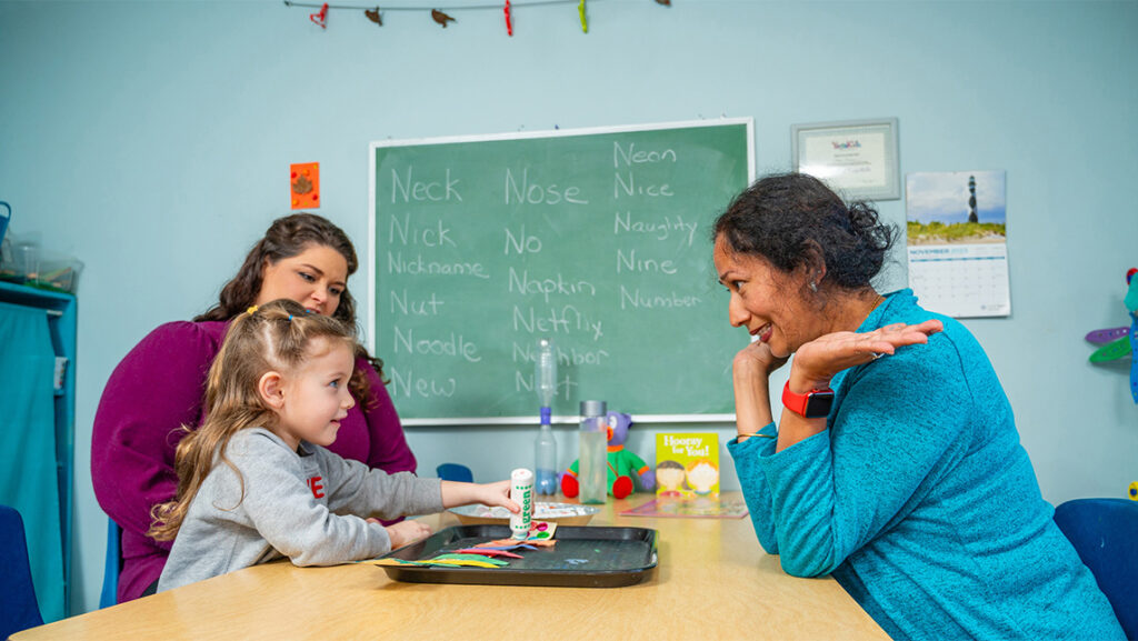 A young girl interacts with a woman across a table.