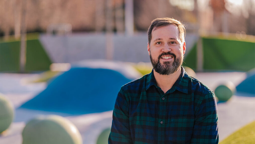 A man smiles at the camera in front of a public park
