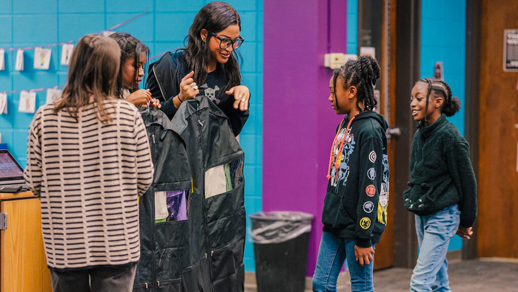UNCG consumer, apparel, and retail studies students Tues-Dé Whethers and Marlowe Harden present a clothing bag to Oak View Elementary students Talia Pryor and Mikayla Cotton.