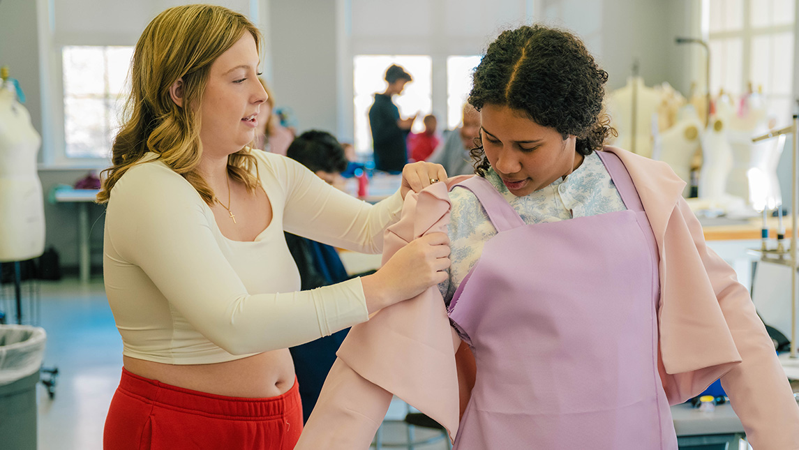 UNCG consumer, apparel, and retail studies student Baleigh Layell puts a jacket on Oak View Elementary student Angie Martinez.