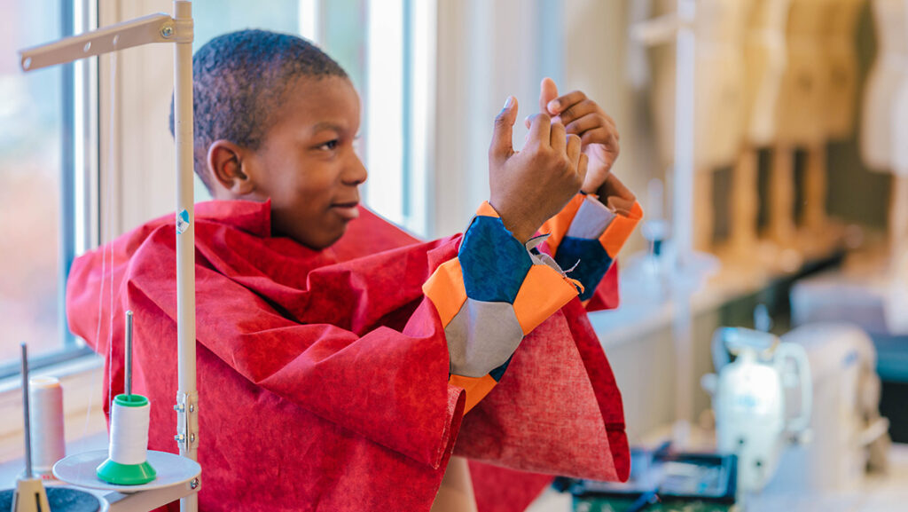Oak View Elementary student Thomas Griffin holds up his arms to check sleeves on a new outfit made by UNCG consumer, apparel, and retail studies students.