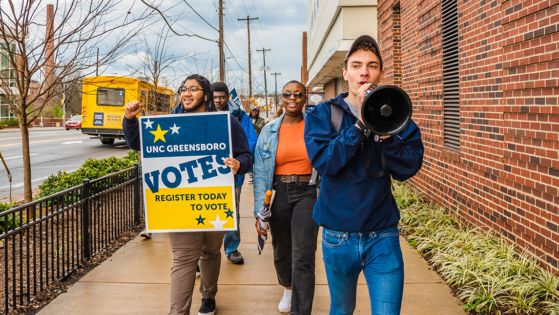 UNCG students carry a vote sign down the street.