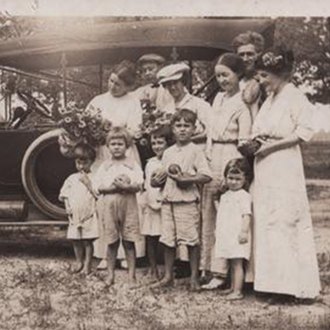 A family posing in front of a car from the early 1900s.