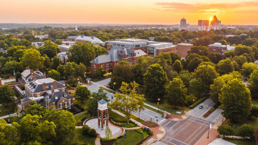 Arial view of UNCG campus with the sun rising behind the Greensboro skyline in the distance.