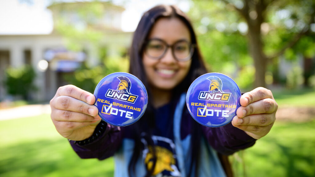 UNCG student holds up voting buttons