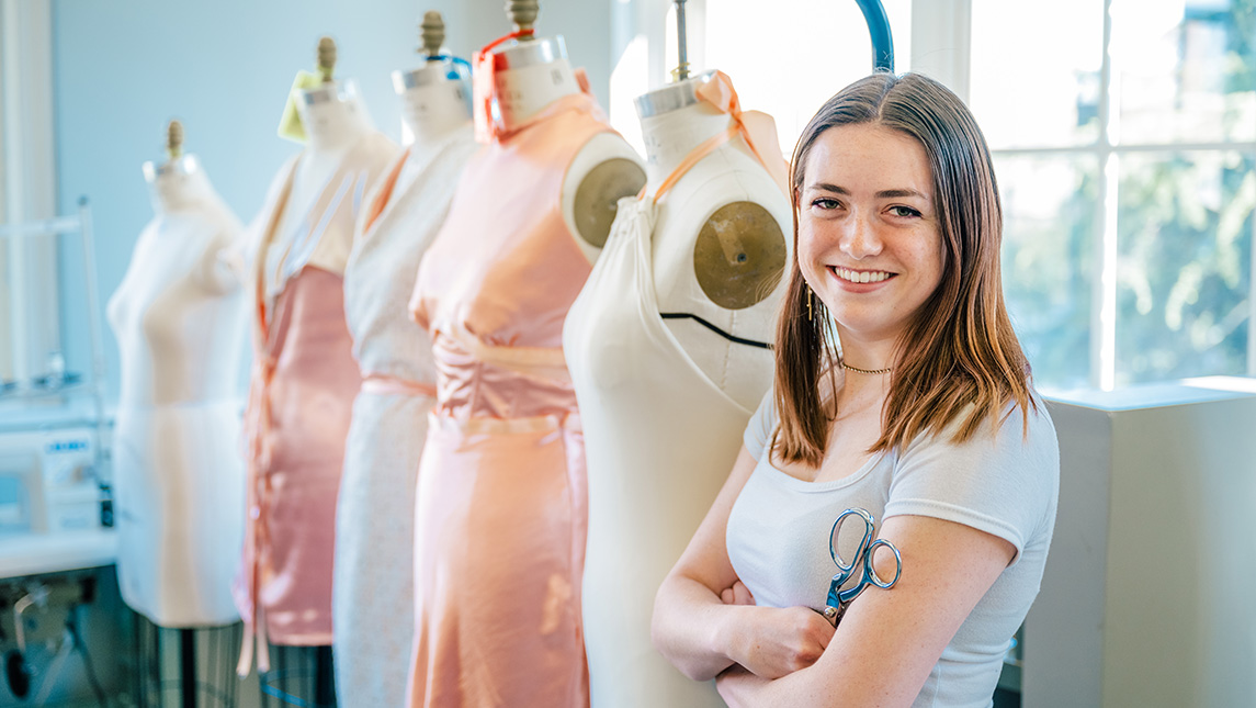 UNCG student Lisa Woolfall stands a row of mannequins with dresses.