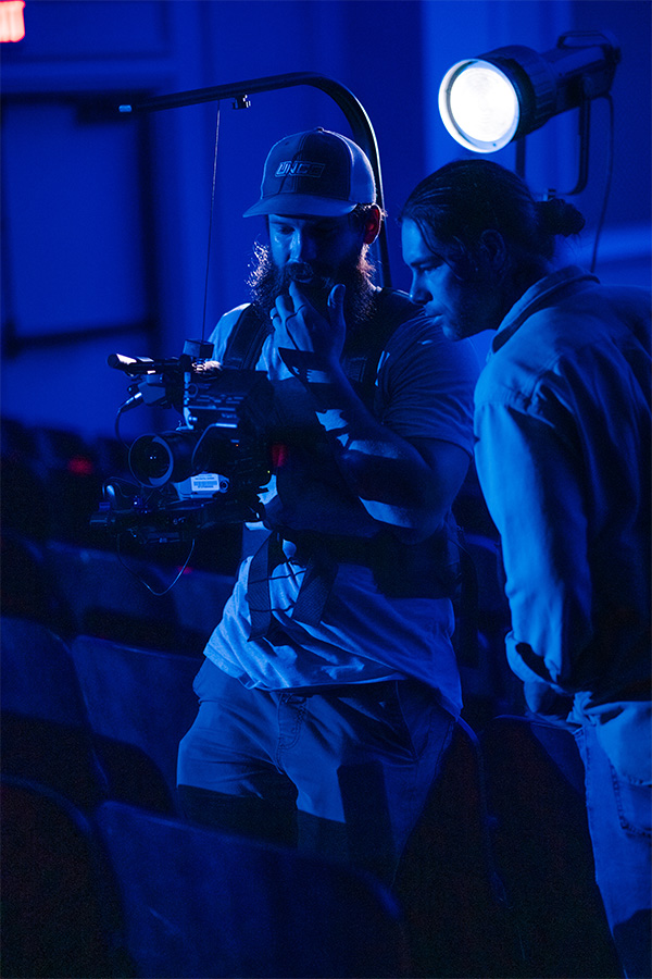 UNCG videographers David Row and Grant Gilliard check the shot in their camera in a dark auditorium.