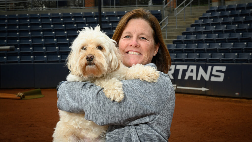 UNCG Softball Coach Janelle Breneman holds a dog on the softball field.