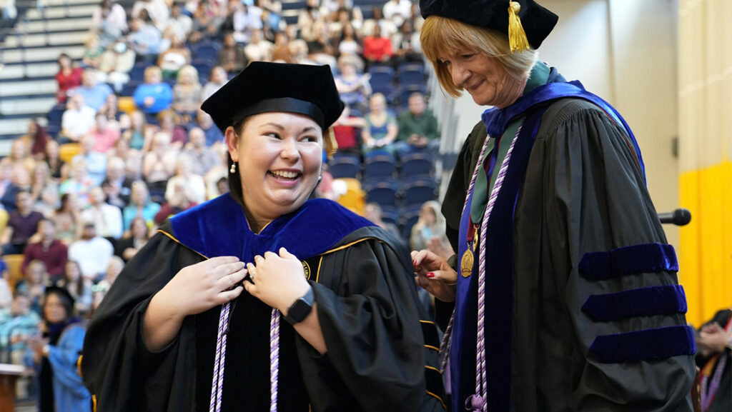 UNCG doctoral student Carrie Doss receives her hood from mentor at hooding ceremony.