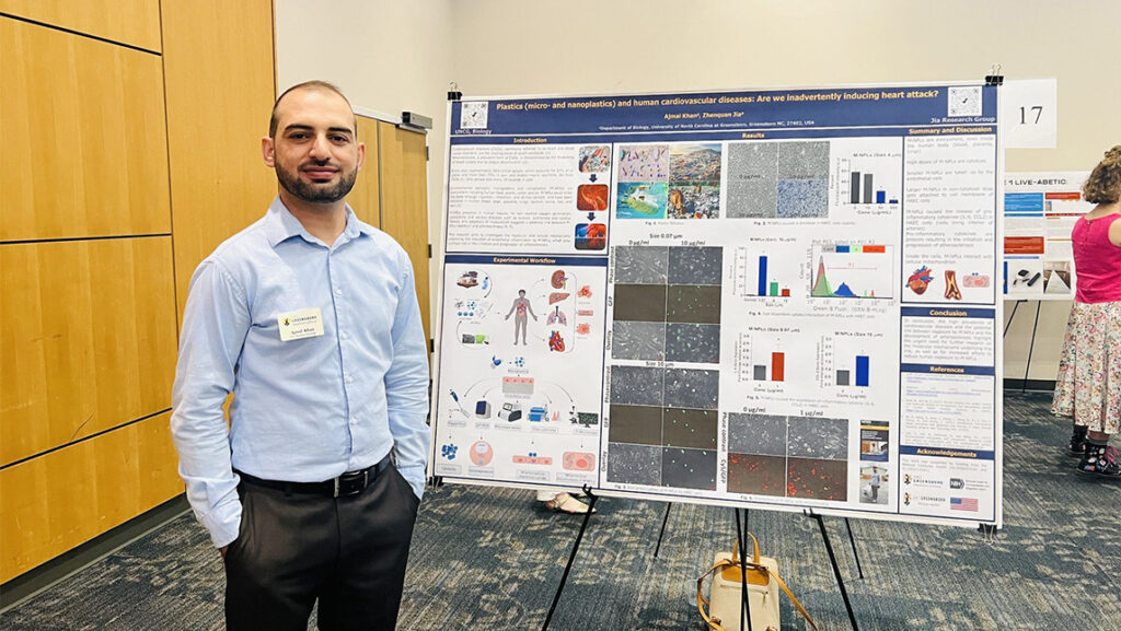 A UNCG graduate school student stands next to his poster at the research and creativity showcase.
