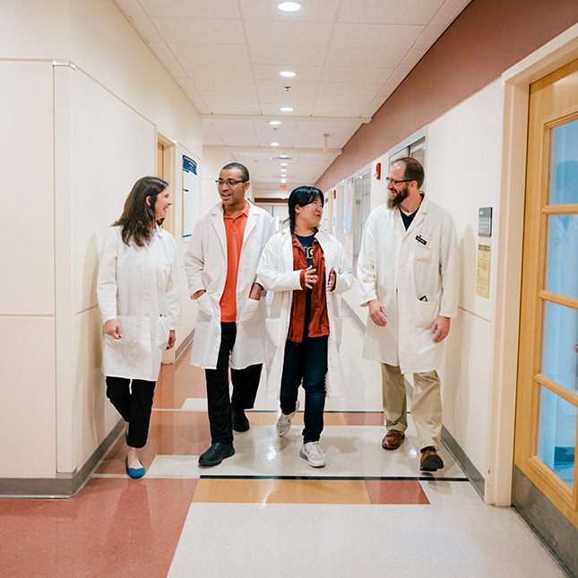2 grad students and 2 professors walk down a hall in the Sullivan building in white lab coats. 