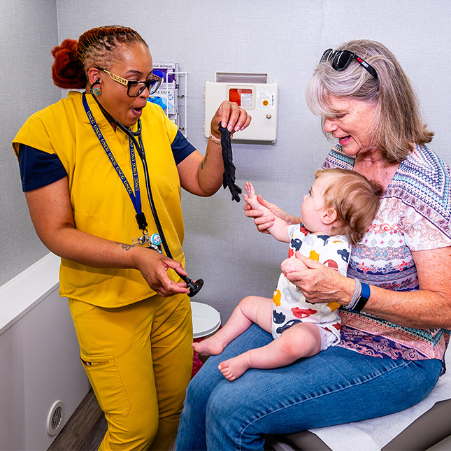 A nurse checks a baby with his grandmother in the Minerva Mobile Health Unit.