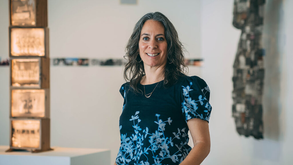 UNCG associate professor of photography Leah Sobsey stands in a room of photo displays.