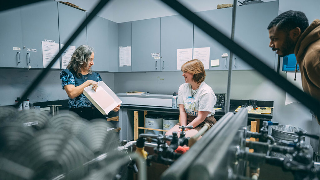Photography associate professor Leah Sobsey shows the anthotype process to students MacK Barber and Antonio Bailey.
