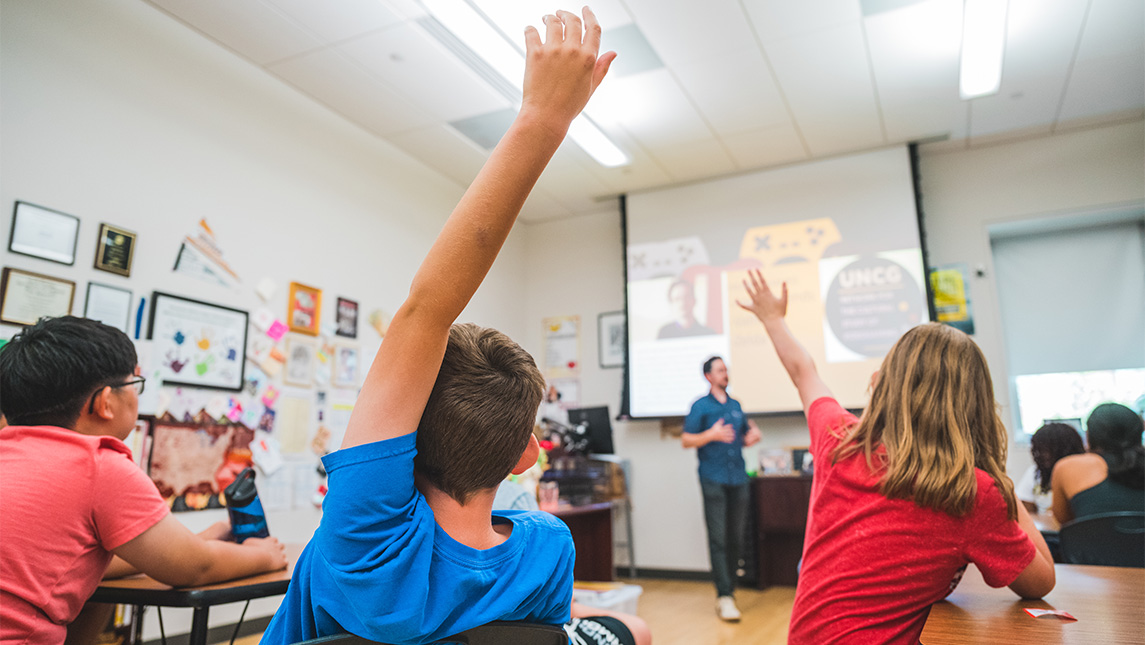 Children raise their hands in a UNCG classroom.