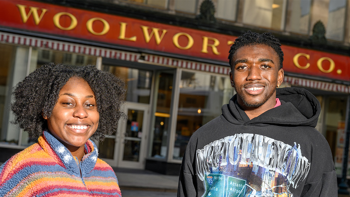 Two students stand in front of a downtown building with a Woolworth's sign.