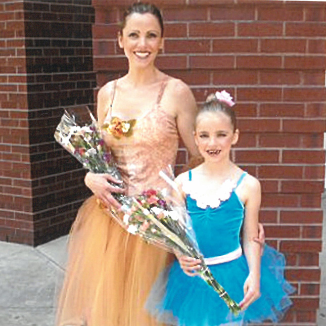 Mother and daughter pose in dance costumes holding flowers.
