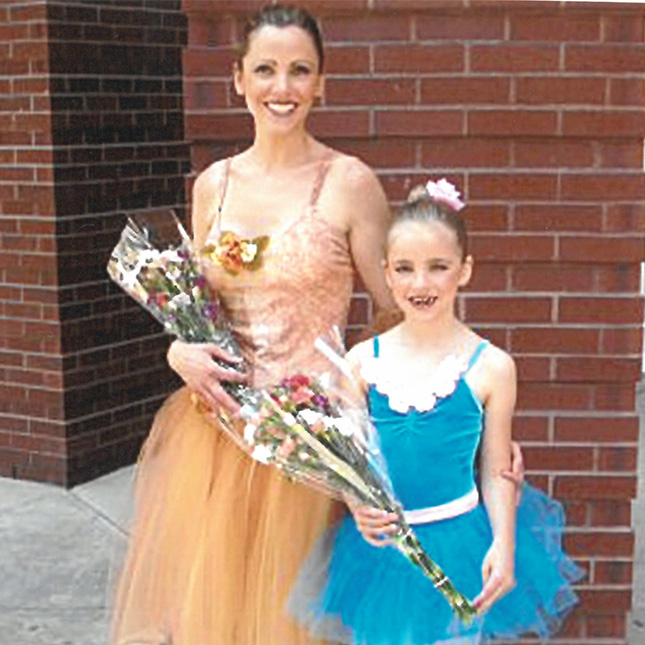 Mother and daughter pose in dance costumes holding flowers. 
