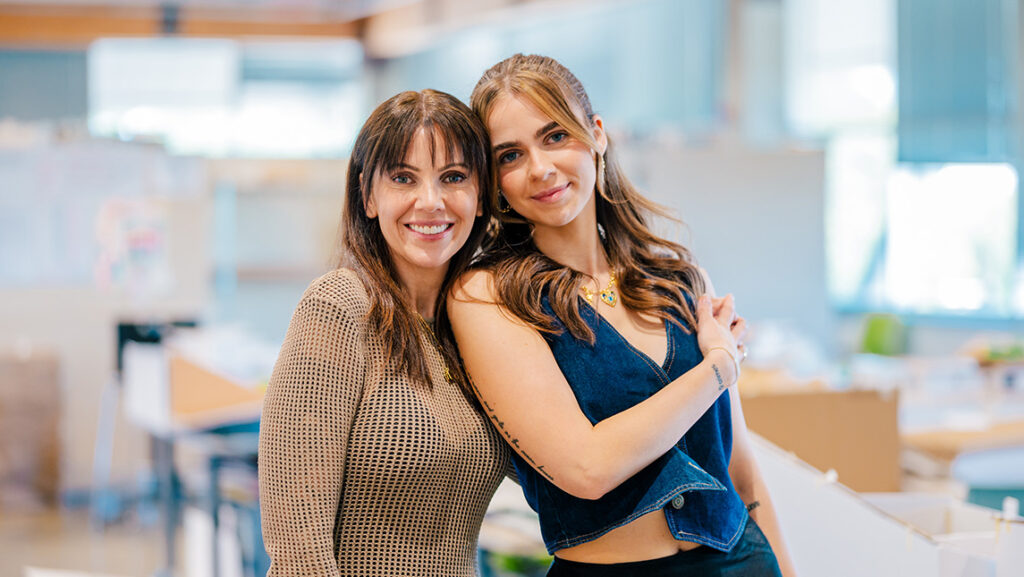 Two women pose affectionately in an art studio.