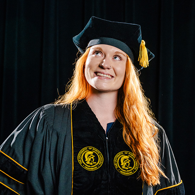 Doctoral grad poses in tam and gown and looks up and to the left.