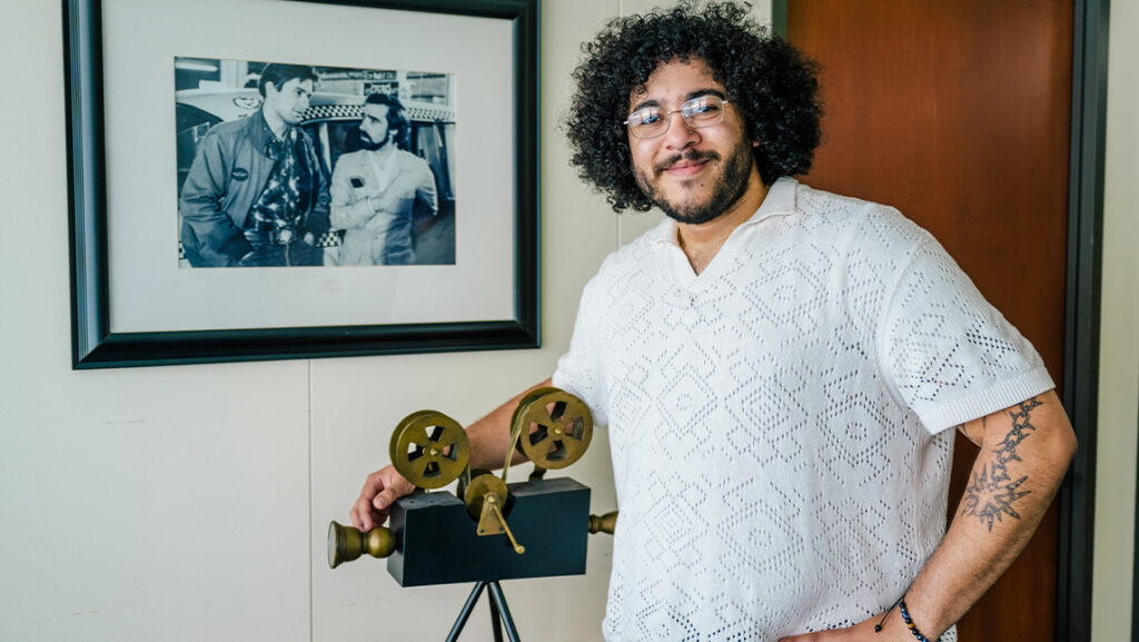 UNCG student Luis Roman stands with camera statue