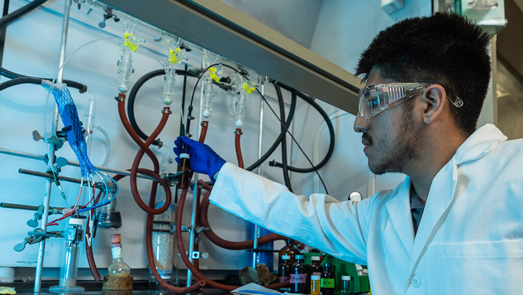 Student in white lab coat works in a chemistry lab.