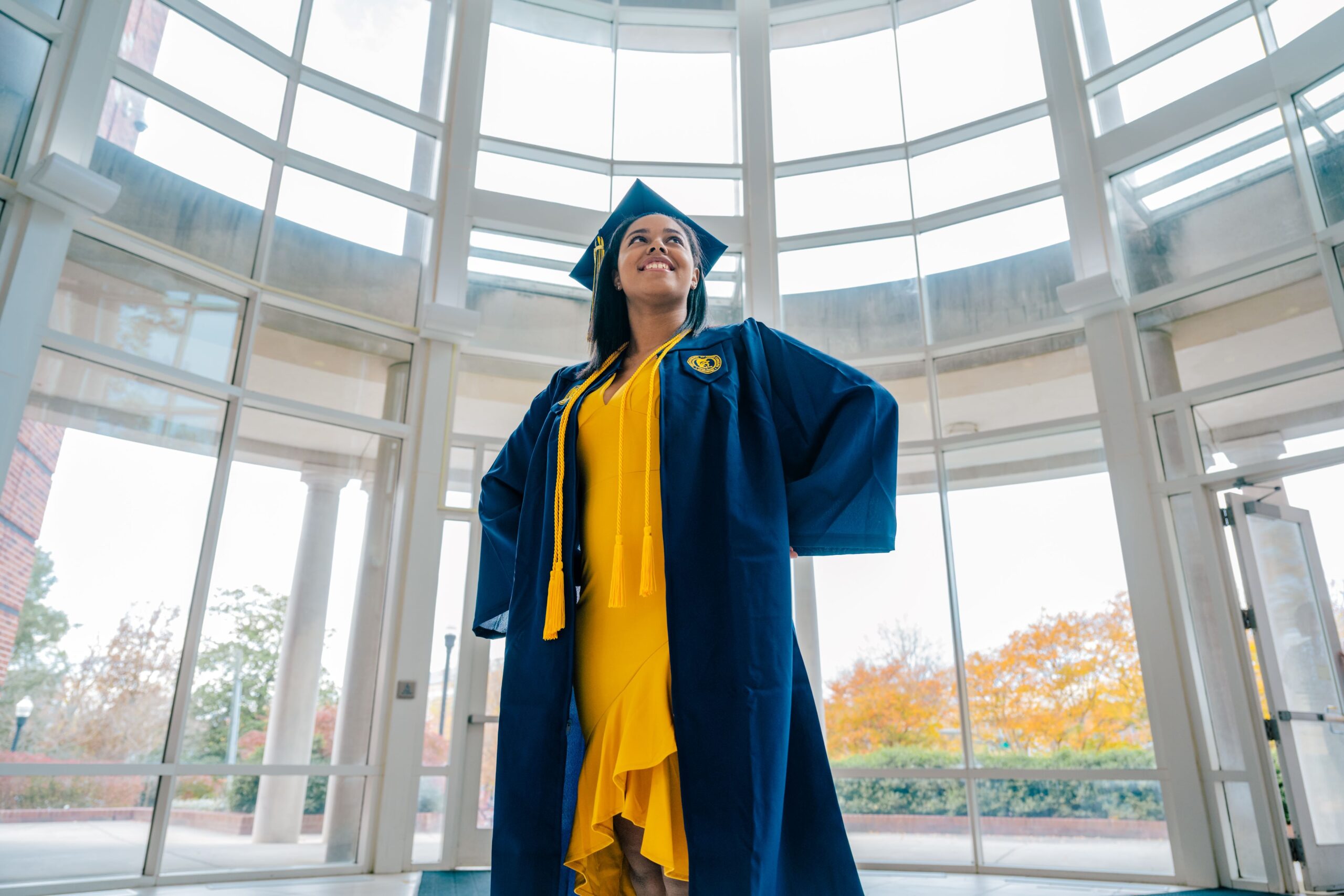 Graduate stands in the lobby of UNCG's humanities building.