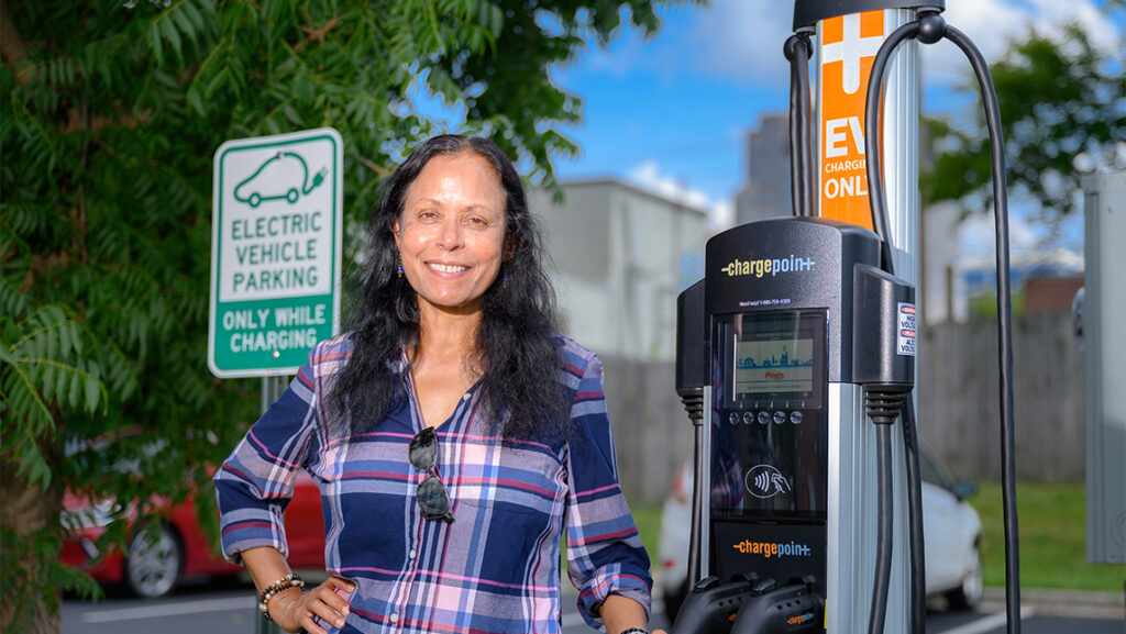 A woman stands in front of an electric vehicle charging station.