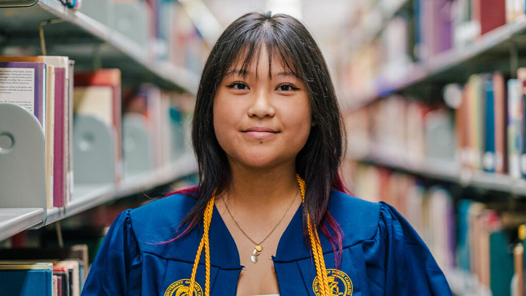 Tiffany Tan stands in her graduation gown among books in the library