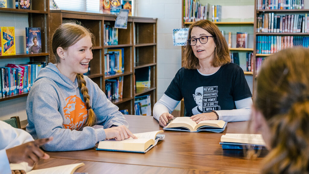 UNCG alumna Dawn Shirk leads a book discussion with students at a table in a library.