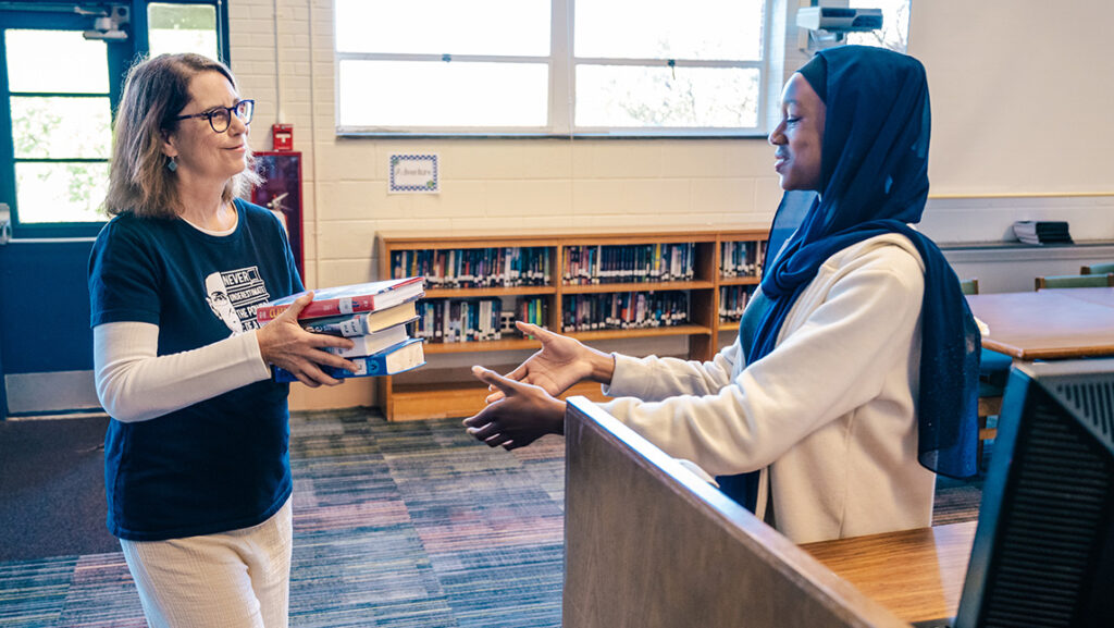 UNCG alumna hands a student a book to catalogue.