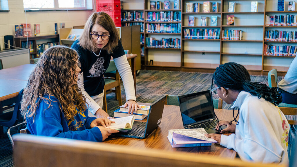 Dawn Shirk, UNCG alumna, looks over a laptop while two middle school students sit at a table.
