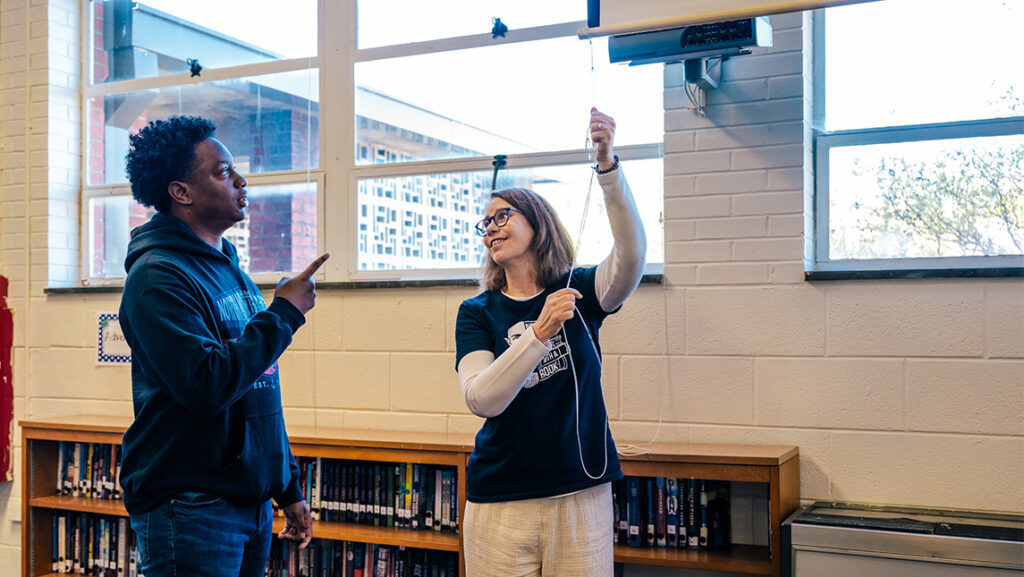 UNCG alumna Dawn Shirk and her library lab technician lower a projection screen.