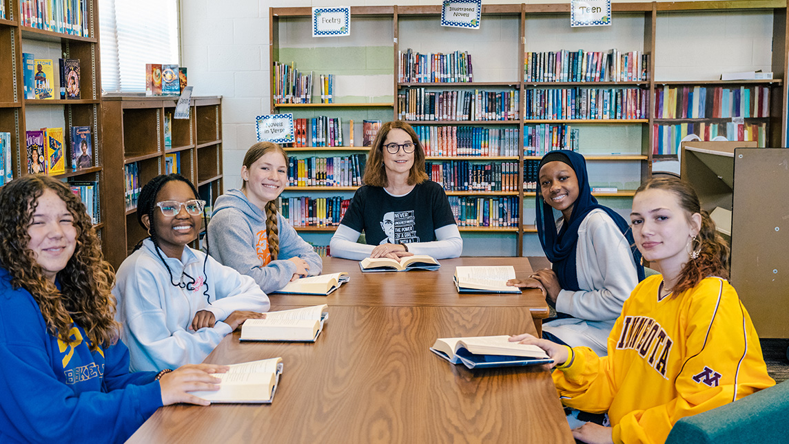 UNCG alumna librarian Dawn Shirk sits at at able with middle school students reading books.