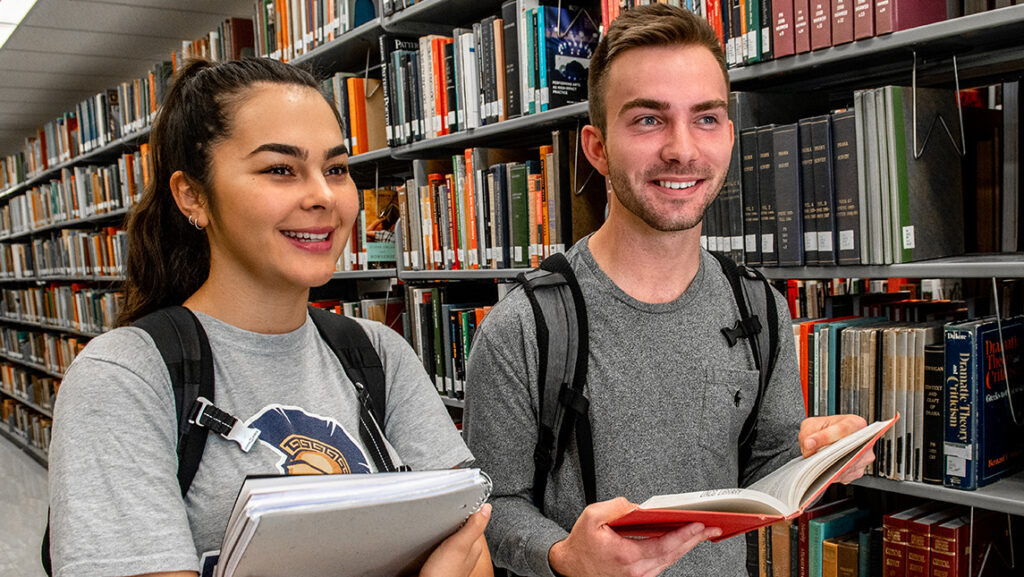 Two students carry books down an aisle in the UNCG library.
