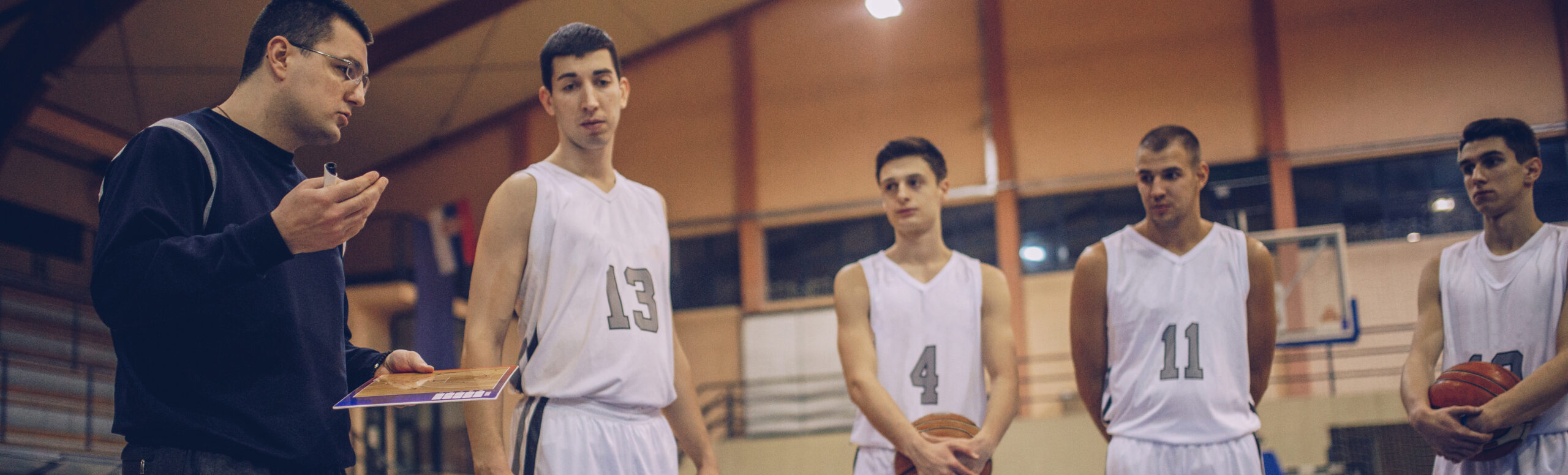 Man talking to boys in sport uniforms holding a basketball.