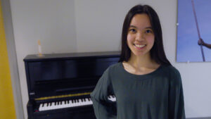 UNCG student Madelyn Good stands by the community piano in Moran Commons.