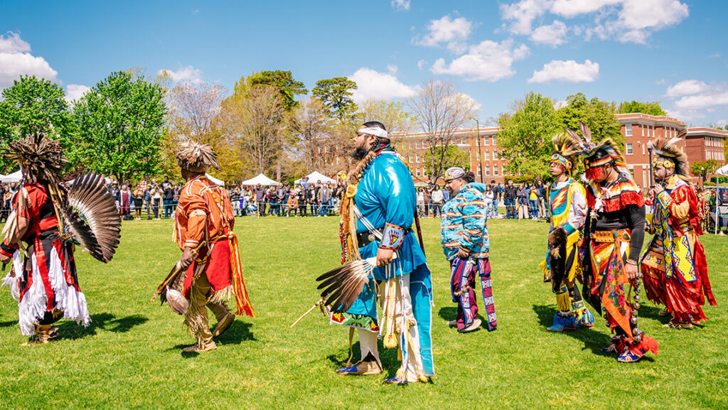 Native Americans in full regalia march across UNCG quad.