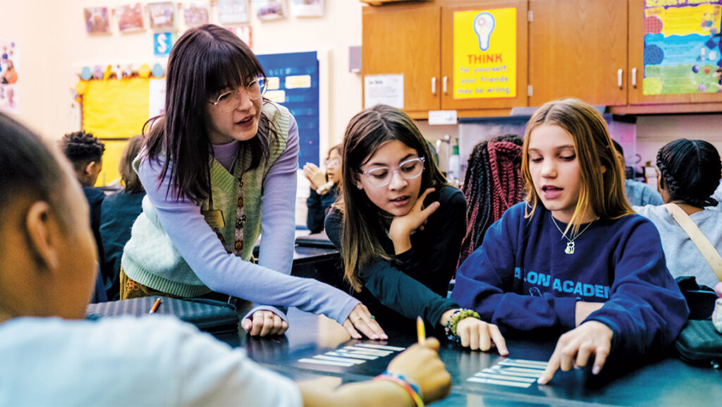 A UNCG student looks over the work of a group of elementary students.
