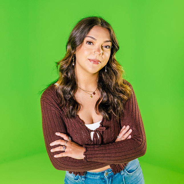 Woman stands with her arms crossed in front of a green screen.
