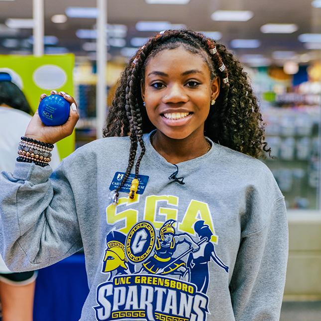 Student in a SGA sweatshirt stands in the EUC holding a ball.
