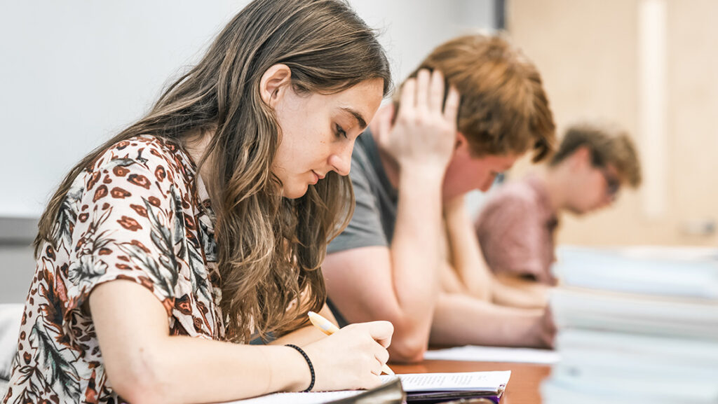 UNCG English students sit at a table writing in their notebooks.