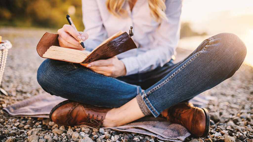 A woman sits outside writing in a journal.