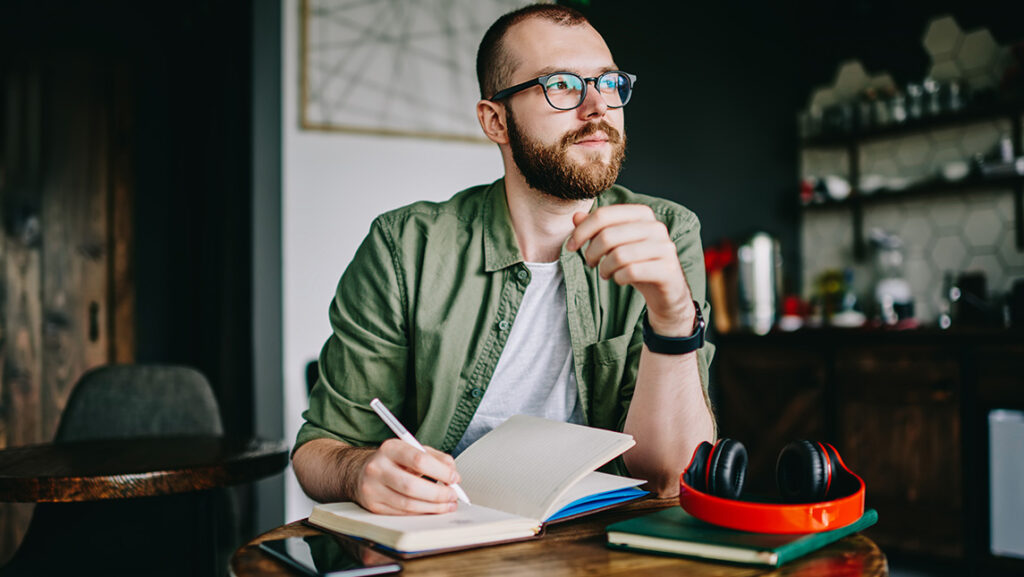 A man looks thoughtful while writing in a notebook.