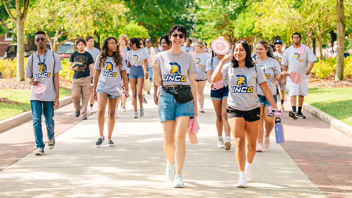 Students walk down College Ave in UNCG t-shirts.