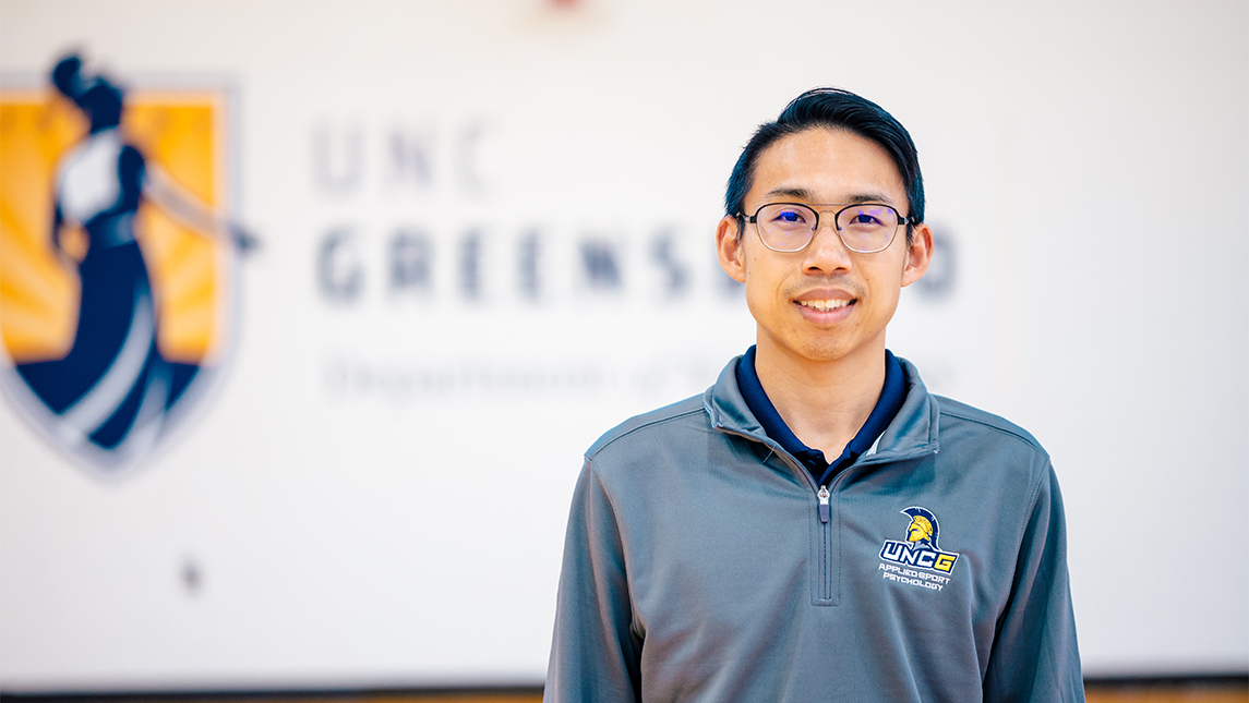 A headshot of a professor with the UNCG logo behind him.