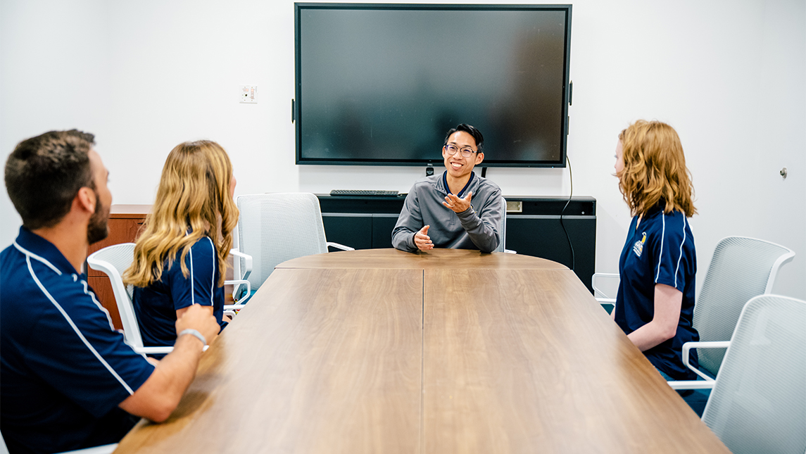 A professor sits around a round table with his students.
