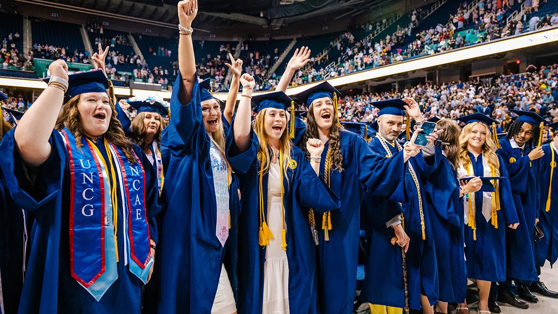 Group of UNCG grads cheering at commencement.