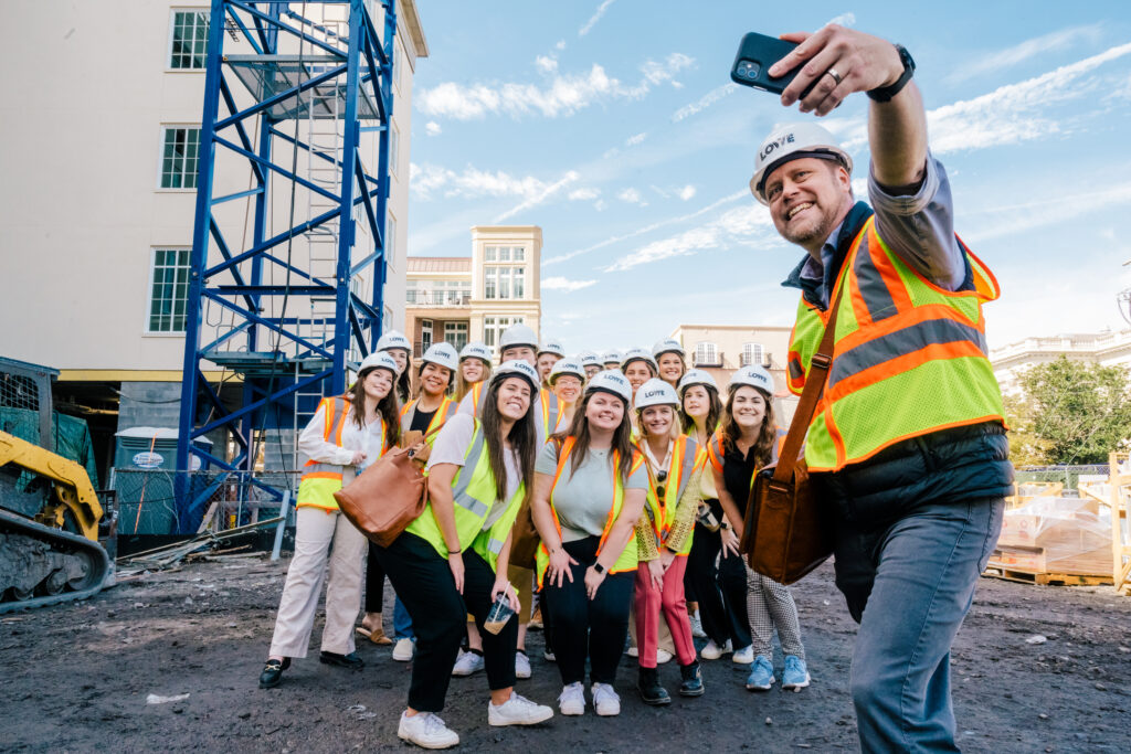 Students in hard hats take a selfie on a construction site.