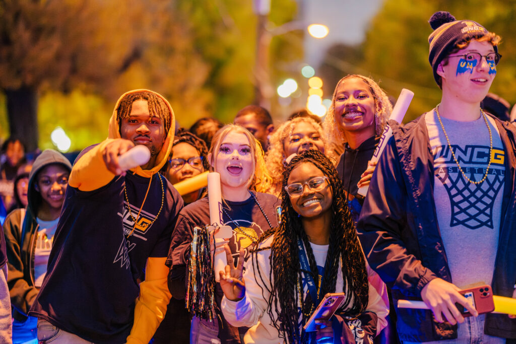 Students walk down a street at night with uncg t-shirts and pom-poms during Storm the Streets.